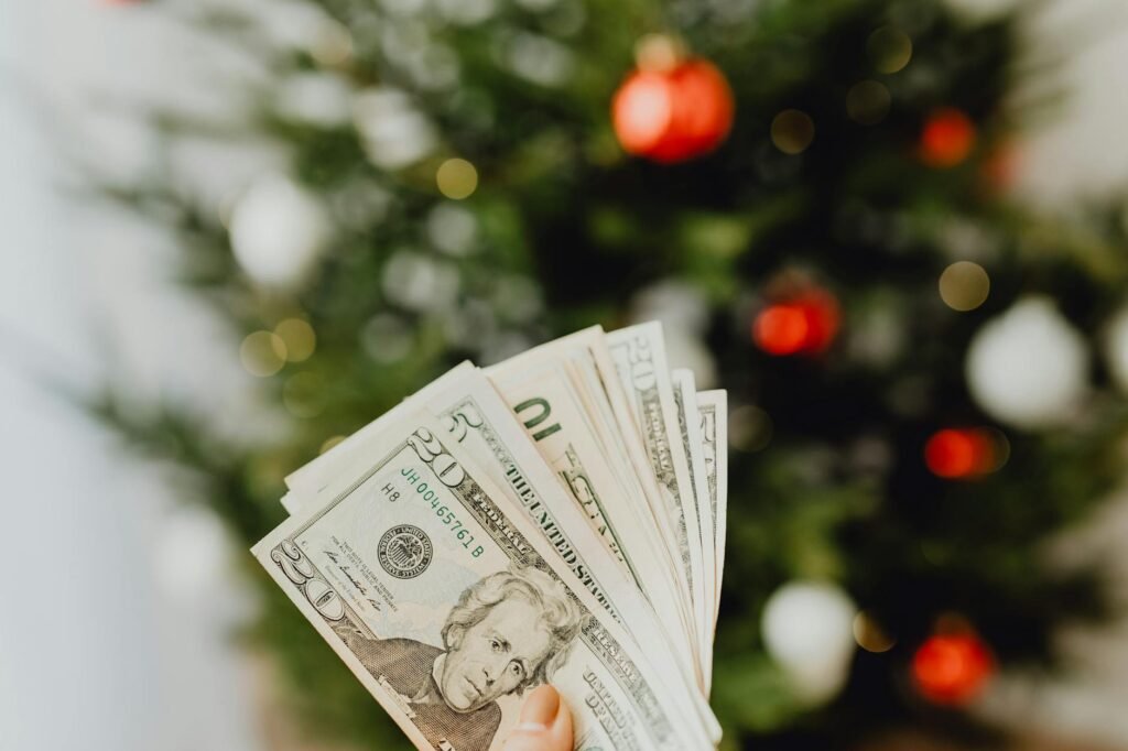 person holding dollar bills with christmas tree in background